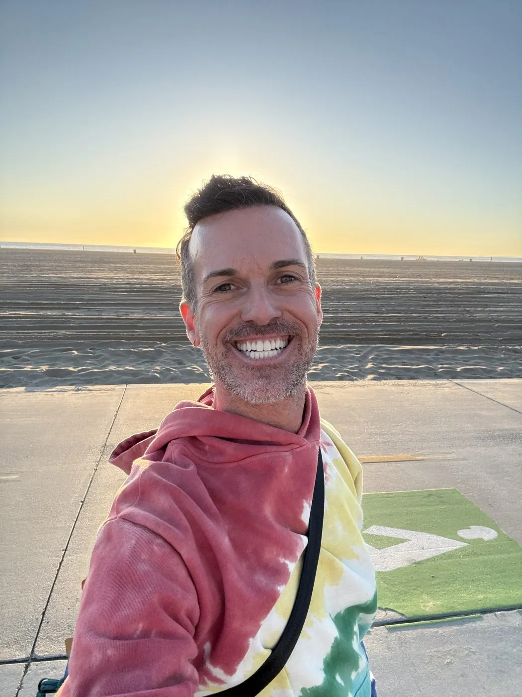 Tino DeMartino smiling at sunset on the beach in a tie-dye hoodie
